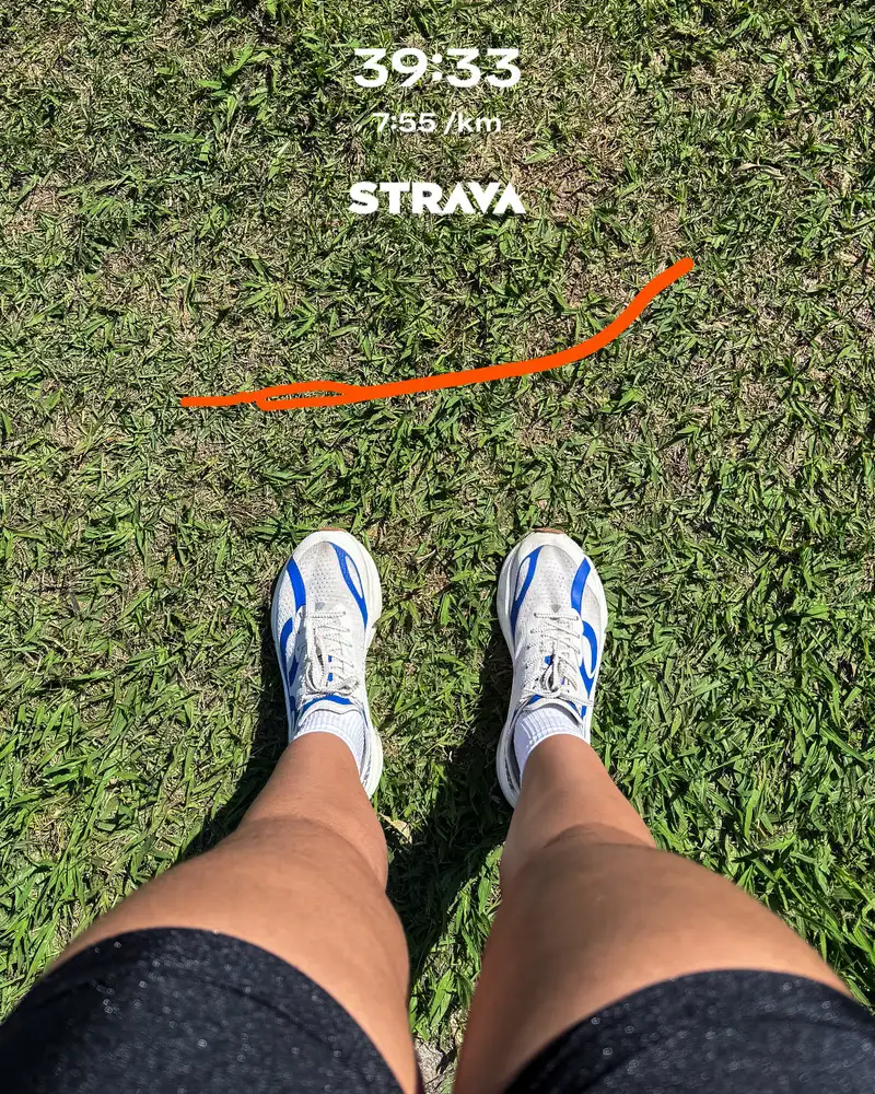 Pés de tênis branco e azul na grama, com o tempo de uma corrida de 5 km registrado no Strava.
