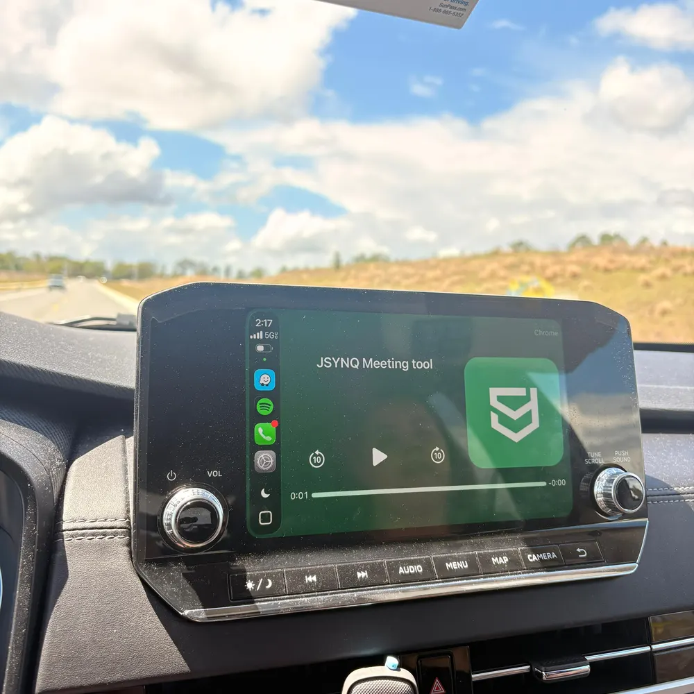 Painel de um carro na estrada com a tela da central multimídia tocando o JSYNQ Meeting tool.